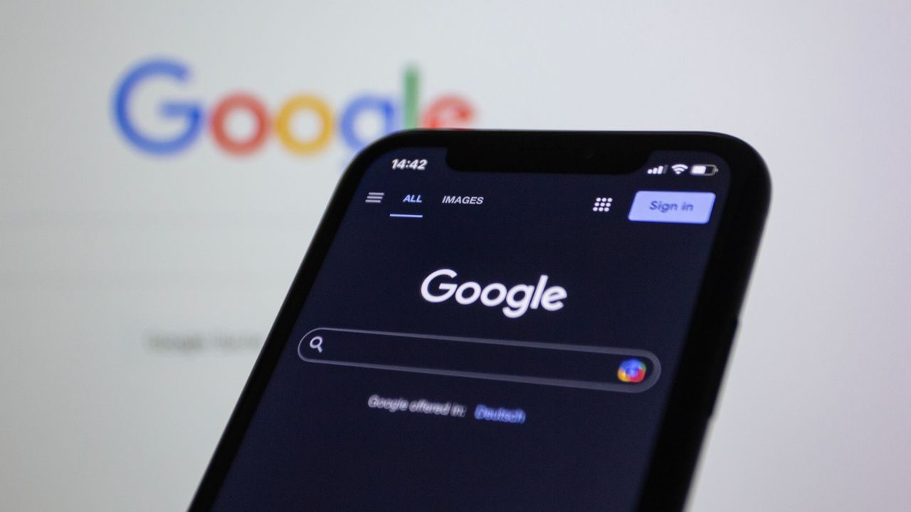 services-04 Écran de smartphone affichant une recherche Google en mode sombre, avec le logo Google en arrière-plan.